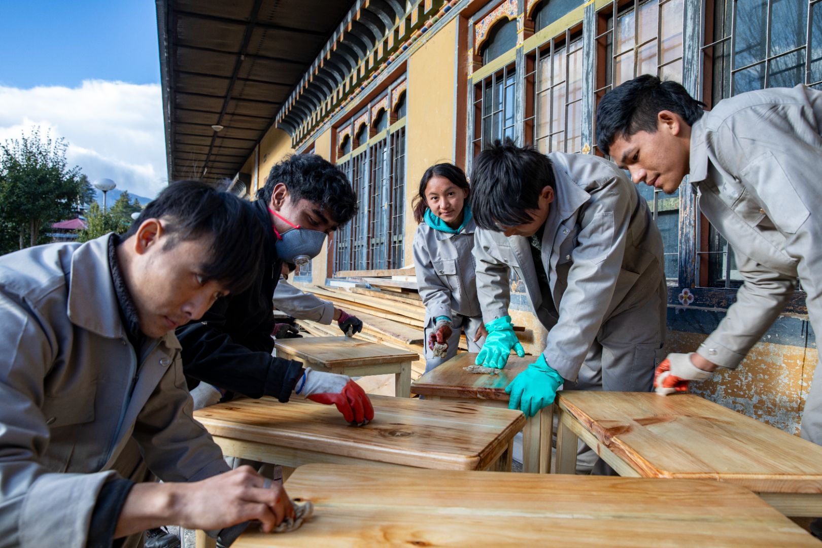 Four men and a woman are putting into practice their vocational skills training in furniture making by sanding the wood at the Technical Training Institute in Bhutan.