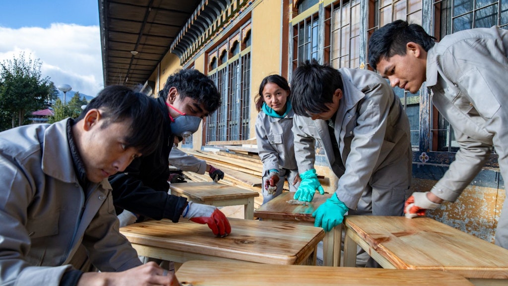 Four men and a woman are putting into practice their vocational skills training in furniture making by sanding the wood at the Technical Training Institute in Bhutan.