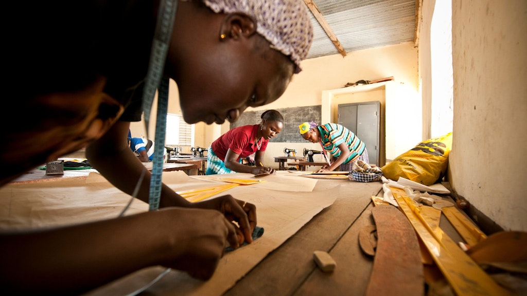 Vocational training in Burkina Faso: A young woman measuring the size of a cloth in a tailoring class with other two women, empowering themselves for a brighter future.