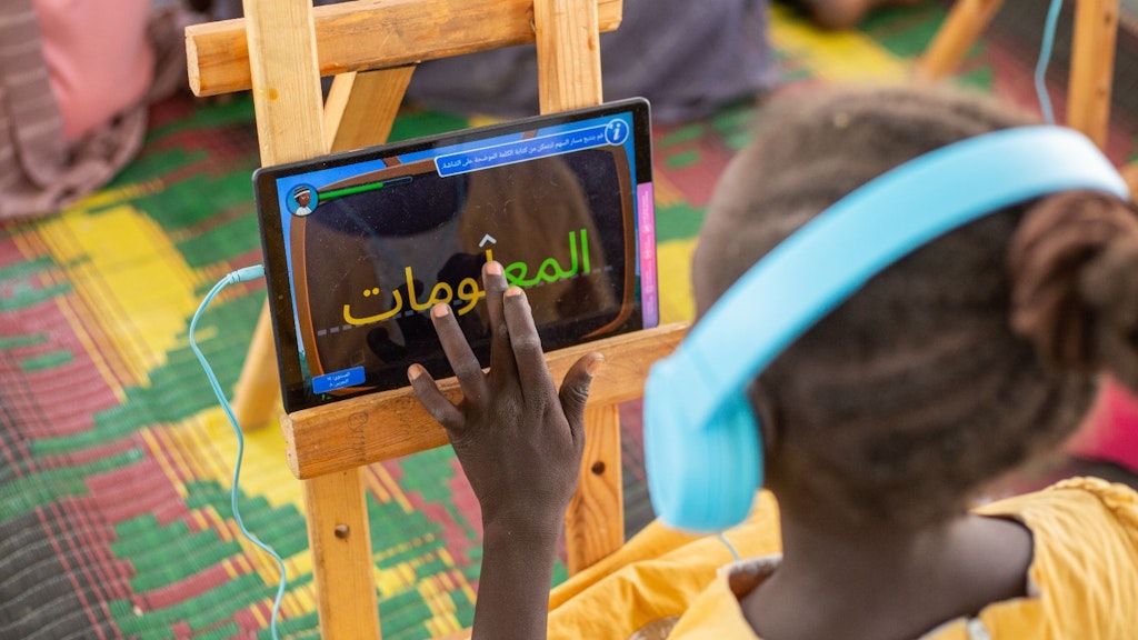 A student wears headphones and writes in a tablet in class