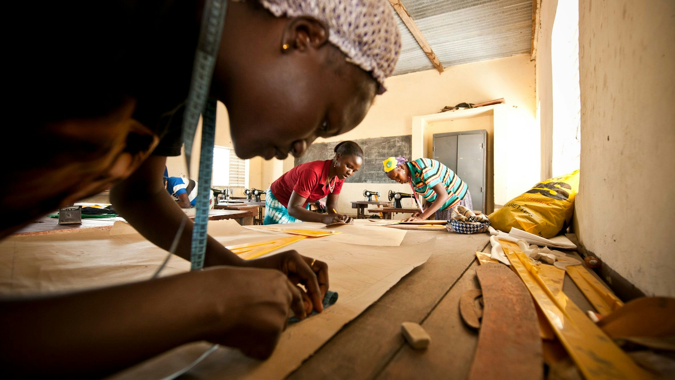 Vocational training in Burkina Faso: A young woman measuring the size of a cloth in a tailoring class with other two women, empowering themselves for a brighter future.