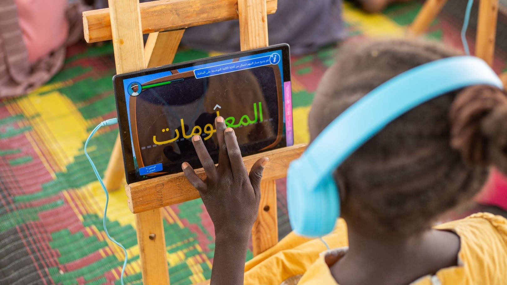 A student wears headphones and writes in a tablet in class
