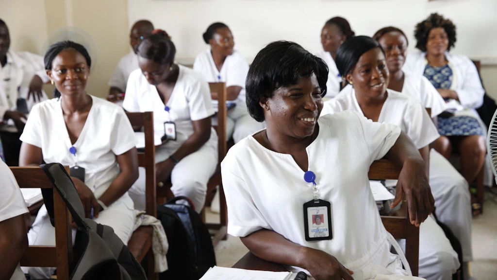Female nurses dressed in white uniforms seated at desks during a training program to learn more about child and adolescent mental health in Liberia.